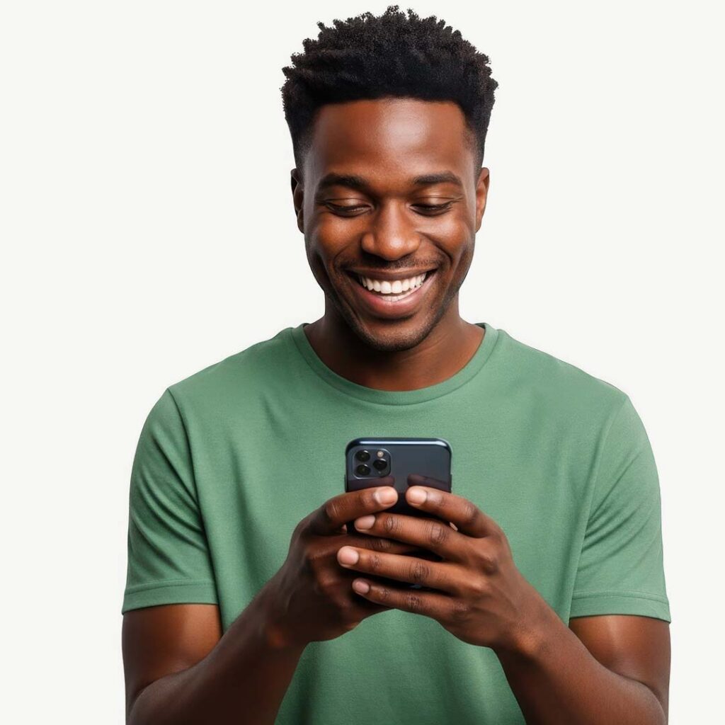 A smiling man wearing a green t-shirt holds a dark smartphone with both hands while looking down at the screen against a white background.