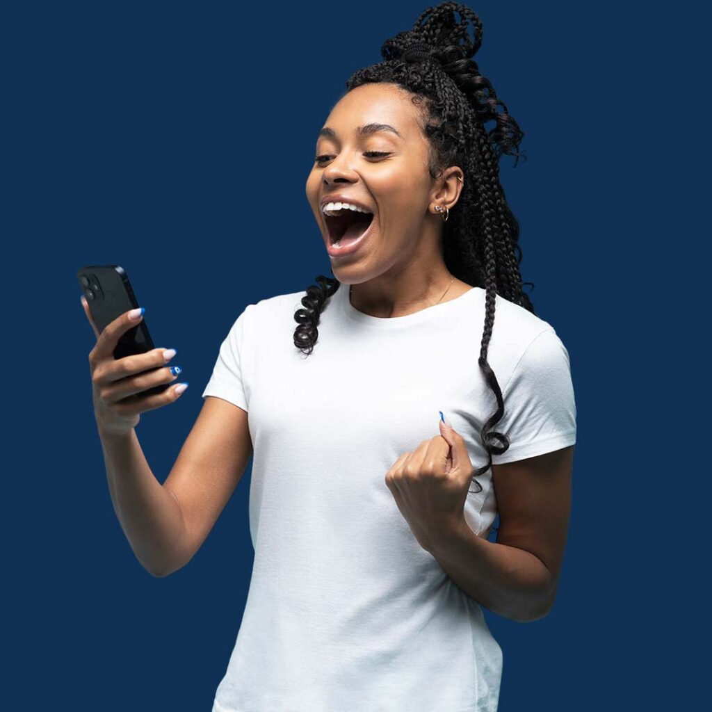 A woman with braided hair wearing a white t-shirt holds a smartphone and smiles with excitement against a blue background.
