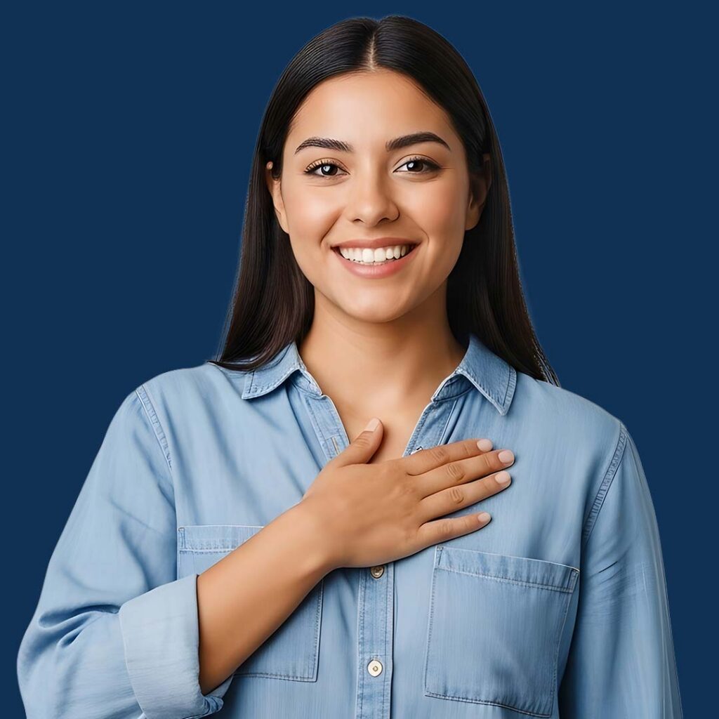 Portrait of a smiling woman with long dark hair wearing a light blue denim shirt, with her hand placed over her heart against a blue background.