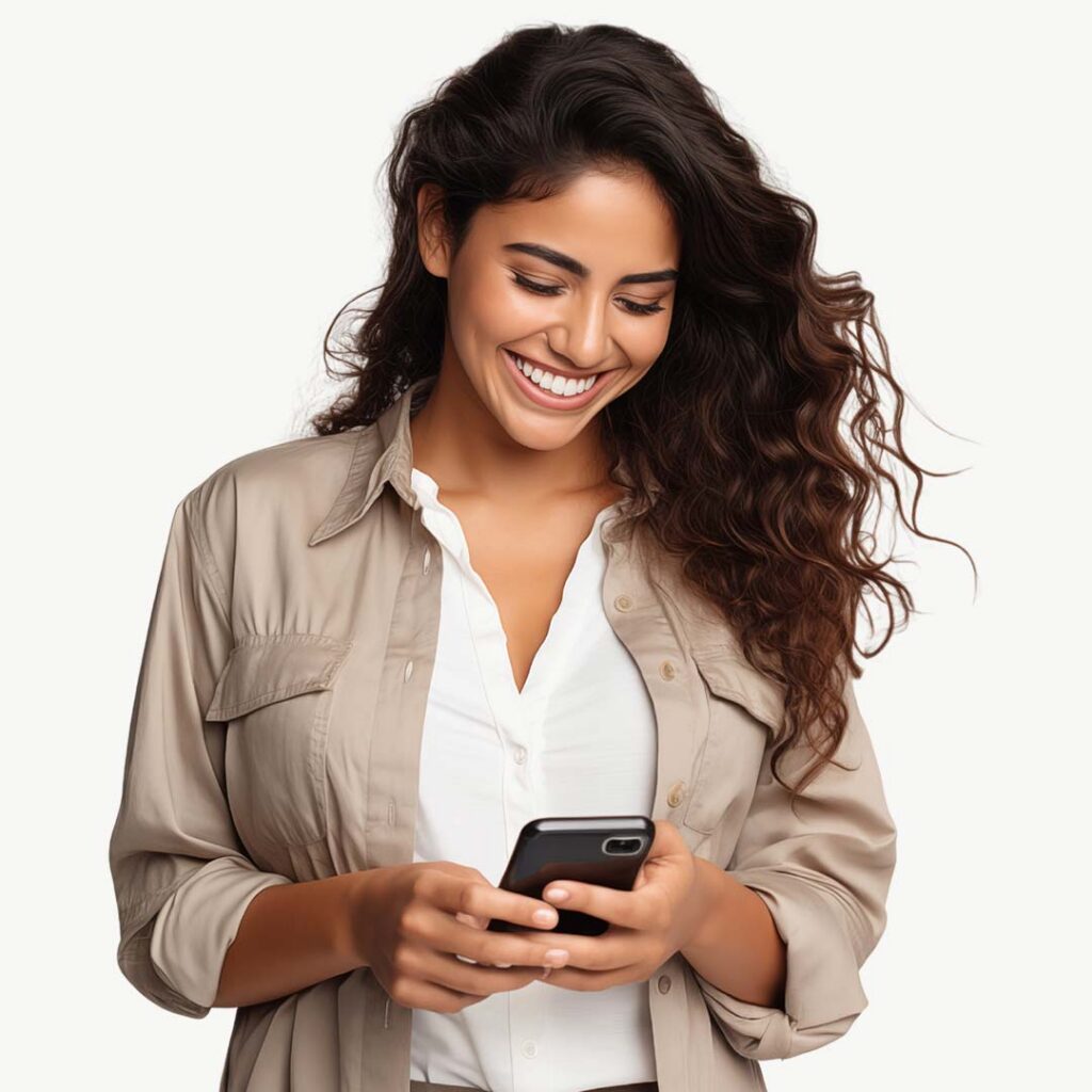 A smiling woman with long dark wavy hair wearing a beige button-up shirt over a white top, looking down at a smartphone she is holding in both hands against a white background.