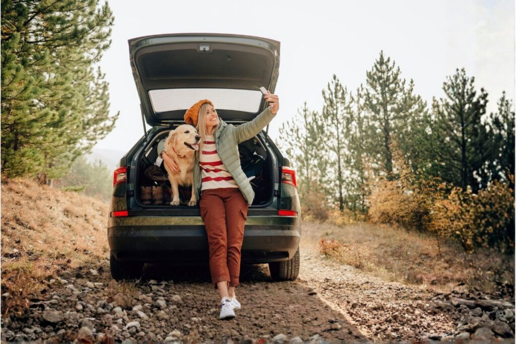 woman taking a selfie with her dog while sitting on the back of her car