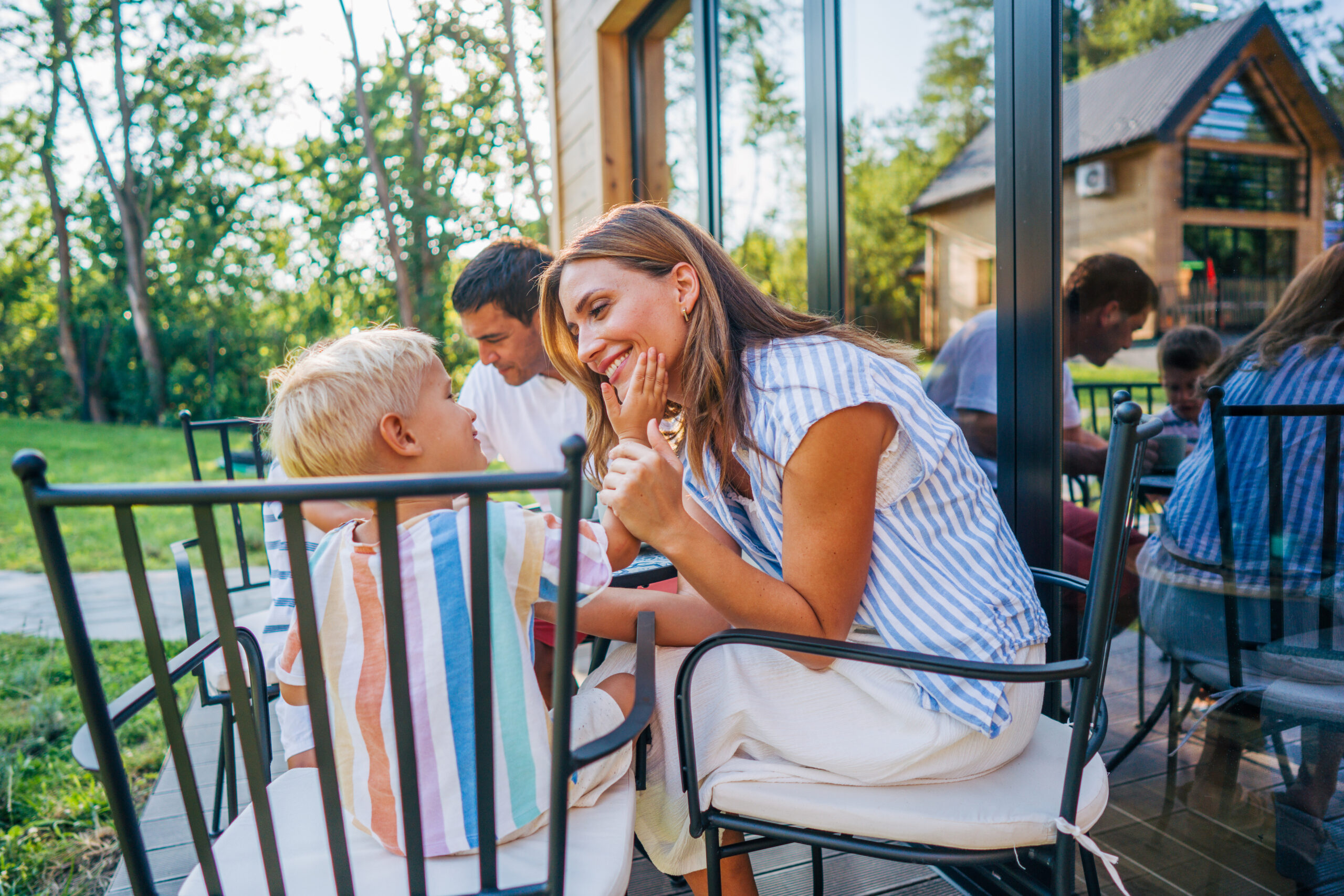 A family of four, consisting of a mom, dad, and their two sons, is spending quality time together on a sunny day. They are seated around a table on the patio of their vacation home.