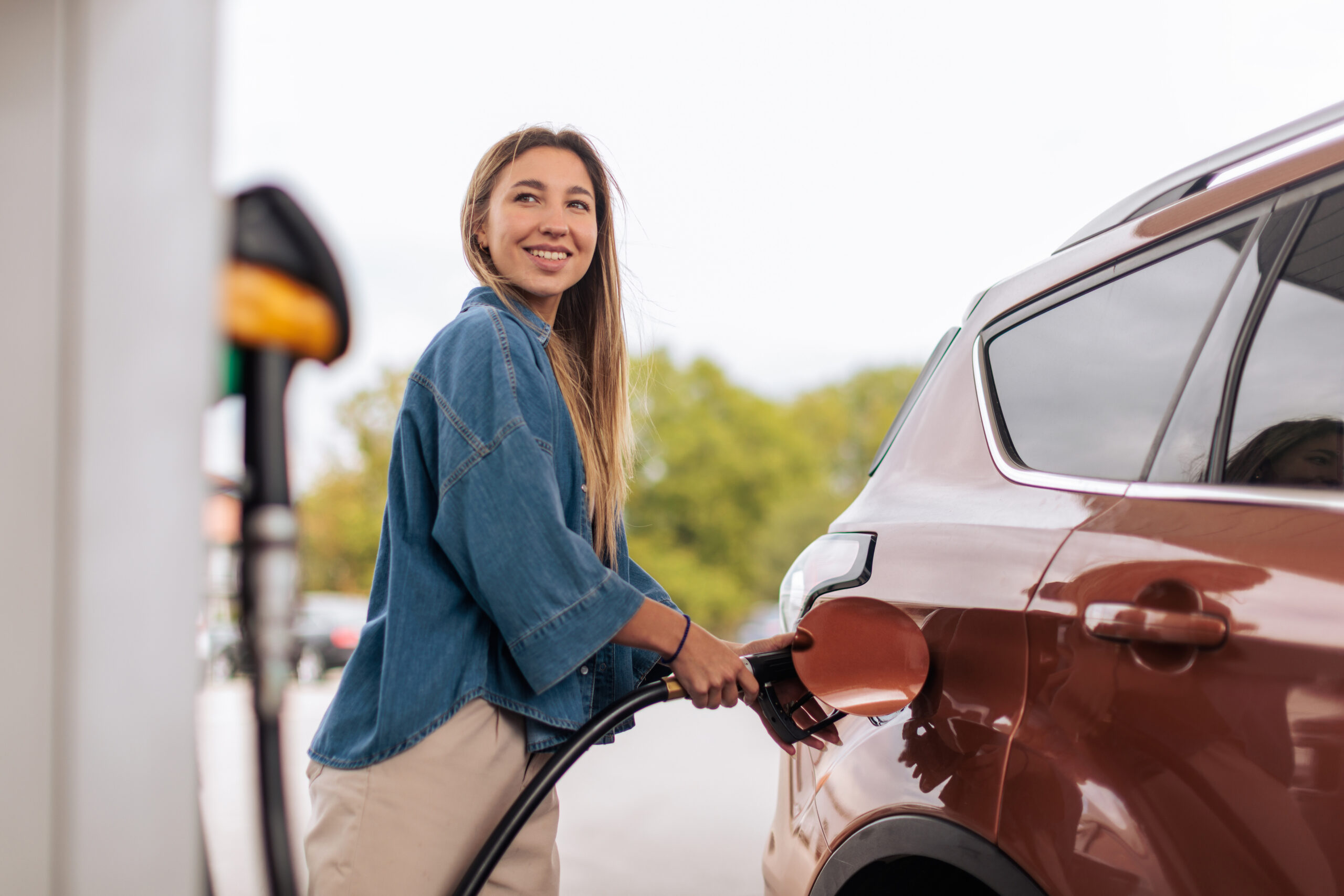Cheerful woman filling her car with fuel at a gas station.