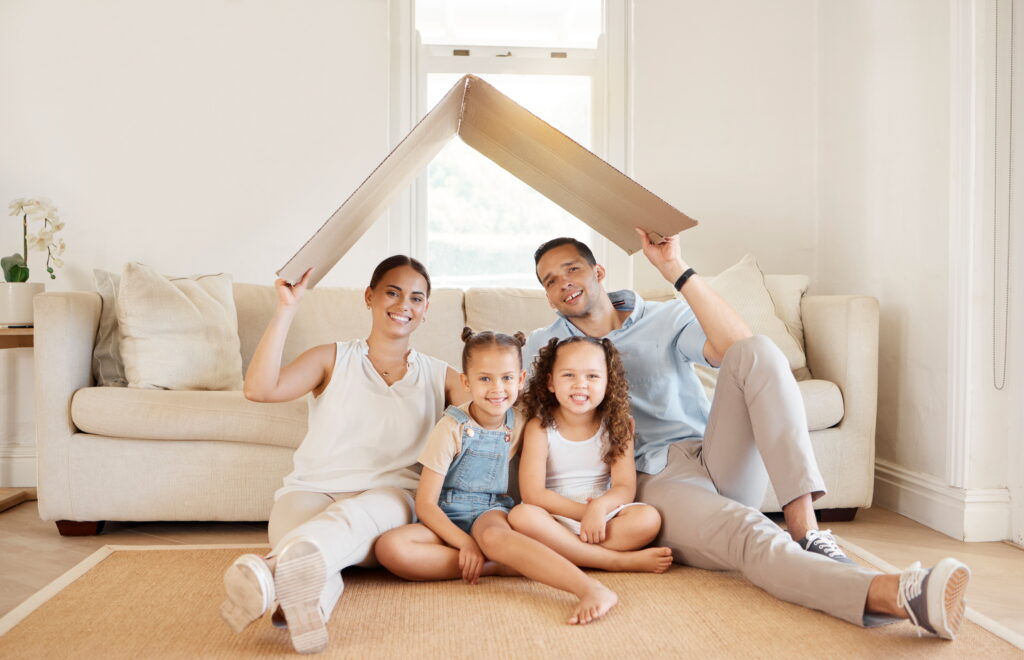 Cardboard roof, family and portrait for home insurance on floor of living room in home together. Mortgage, safety or security with mother, father and children in apartment for property investment