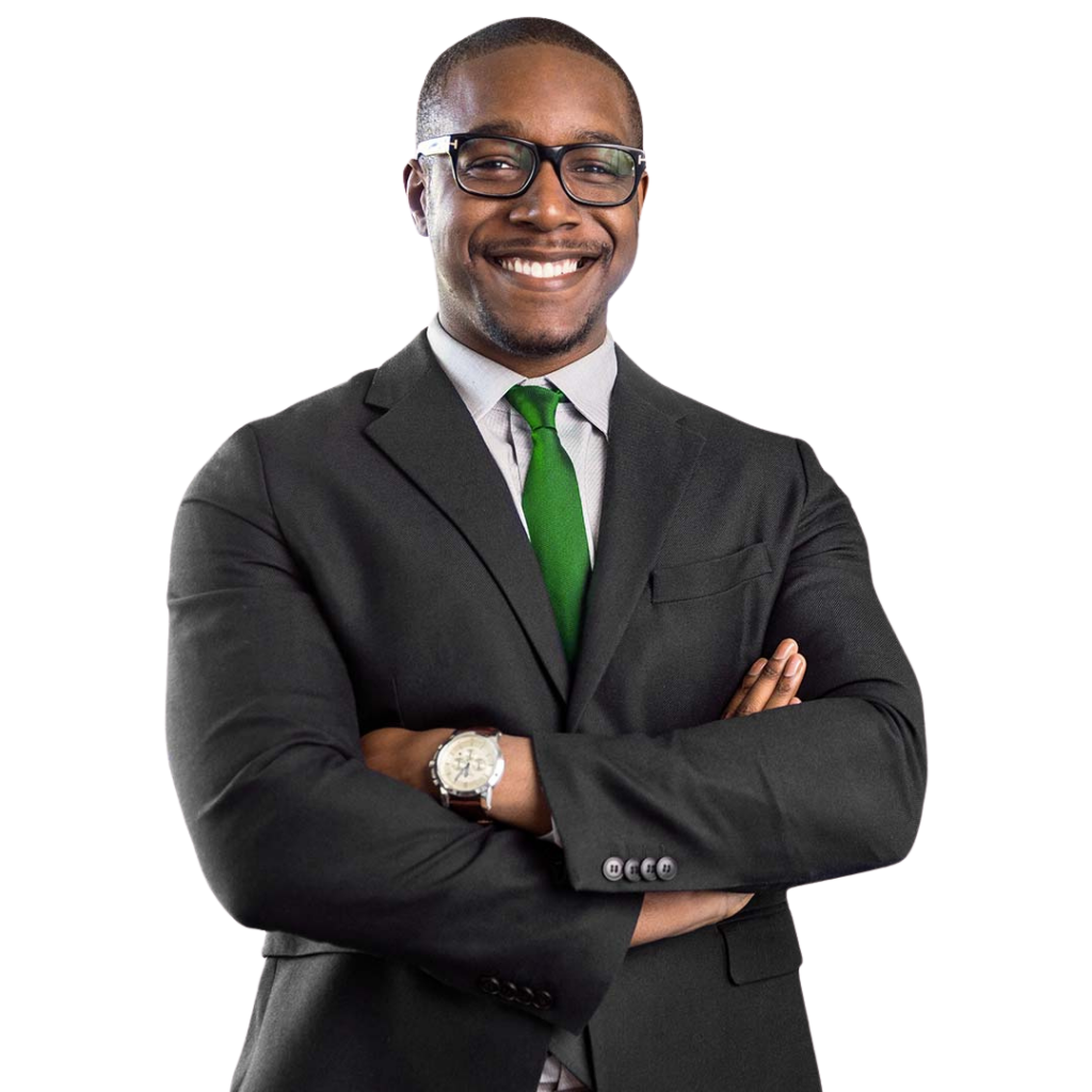 Professional headshot of a smiling man wearing a dark charcoal suit, light blue dress shirt, and green tie, with glasses and a watch, standing with arms crossed against a white background.