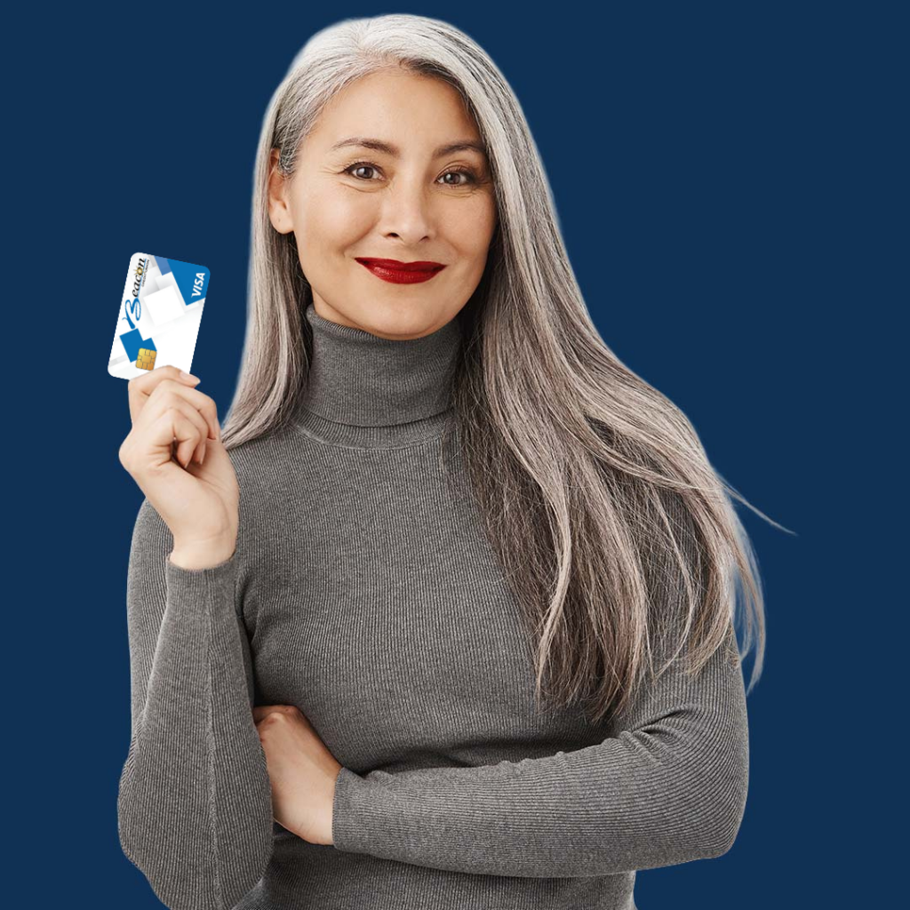 A smiling woman with long gray hair wearing a gray turtleneck sweater holds up a white rectangular device against a blue background.