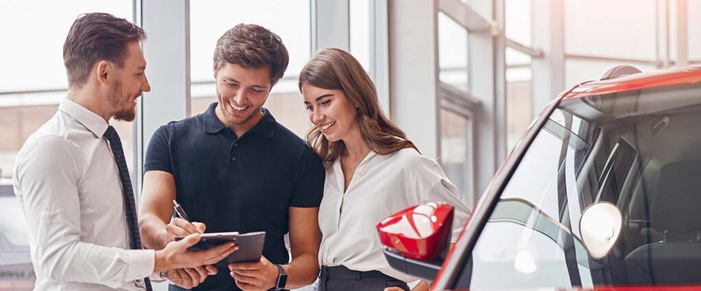 man and woman at car dealership signing car loan paperwork