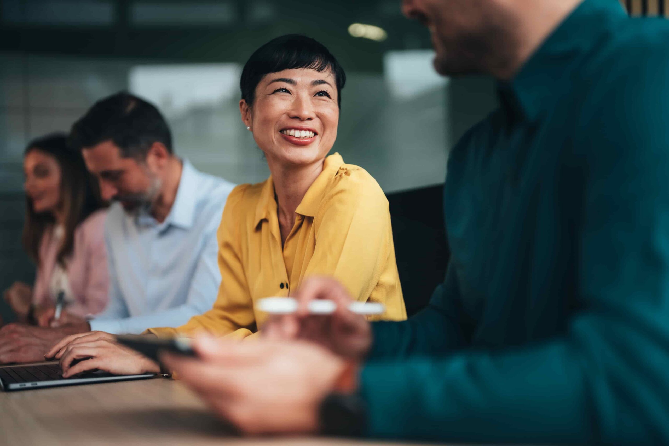 Asian woman in yellow shirt sitting at desk with co-workers