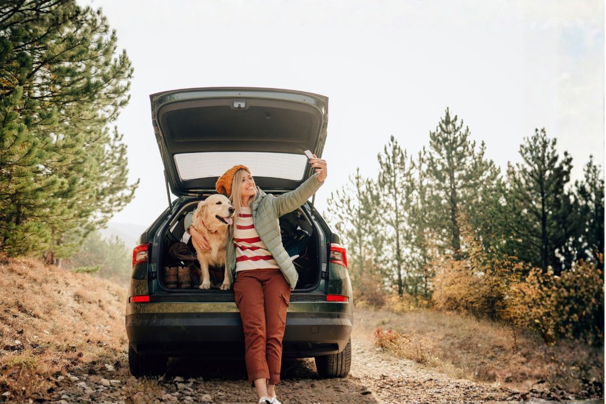 woman taking a selfie with her dog while sitting on the back of her car