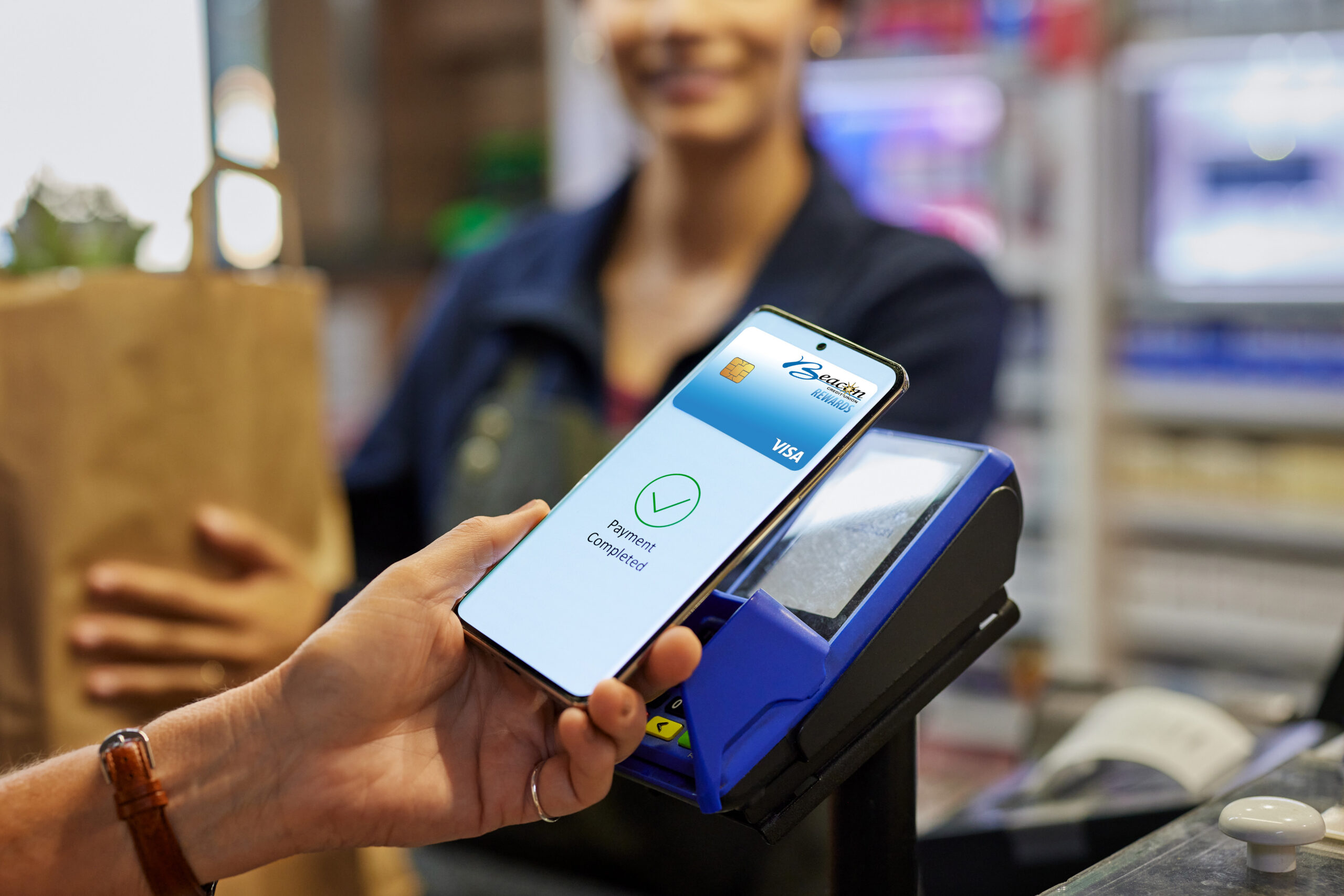 Customer making contactless payment using smartphone at retail counter. Close up of mobile phone displaying completed payment notification. Woman making digital payment at grocery store with mobile phone.