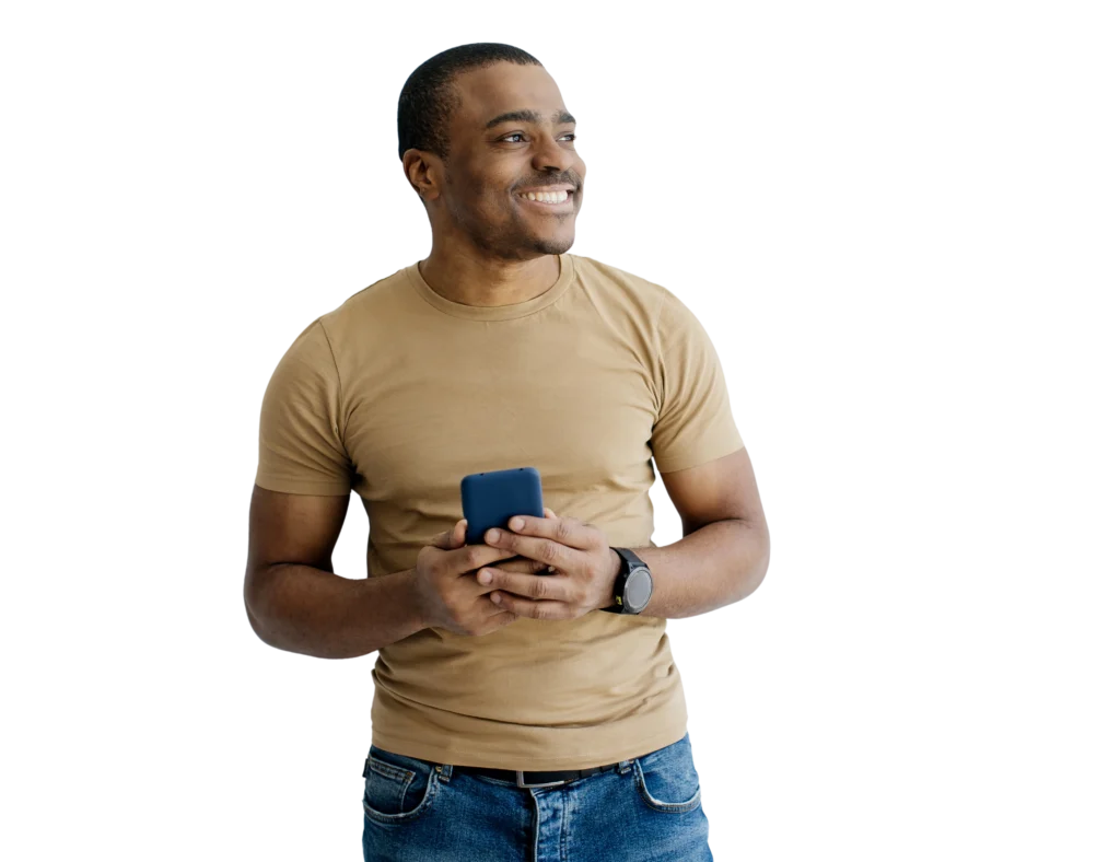 A smiling man wearing a tan t-shirt and jeans holds a blue smartphone in his hands while looking to the side against a white background.